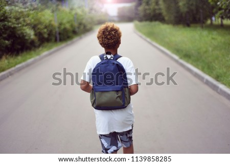 Portrait of the cute african american boy who is going to school with his school  backpack. Student mixed boy on his way to the school. Study for children. Road. Shooting on the july 2018.