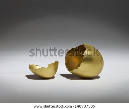 A golden egg is cracked open and empty in a spotlight.