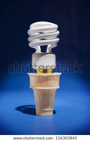 A compact fluorescent  light bulb sticks out of an ice cream cone in a spotlight.