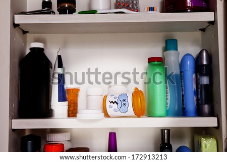 An empty pill bottle with a frowny face lies on a shelf in a medicine cabinet.