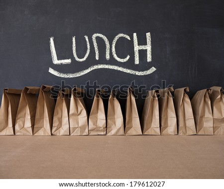 A row of brown bags against a blackboard with the word \'lunch\'.