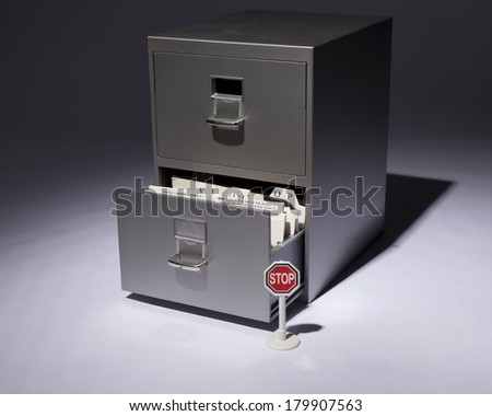 An office filing cabinet in a spotlight with bottom drawer open.