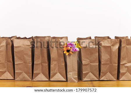 A row of brown paper bags with a flower bouquet in one bag.