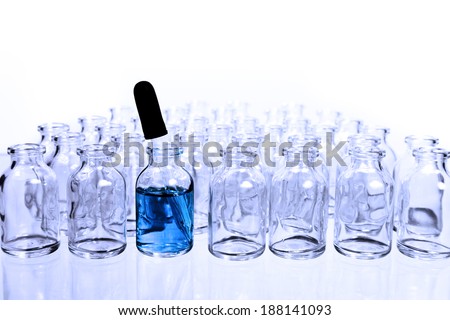 A collection of many small empty scientific vials in rows with a single eye-dropper in one of the containers that has a blue liquid in it,  tinted with a cool blue filter.