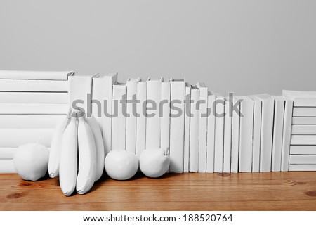 An arrangement of all white books on a wooden table with painted white fruit against a light grey background.