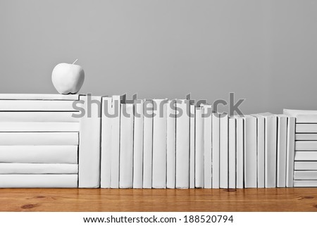An arrangement of all white books on a wooden table with painted white fruit against a light grey background.