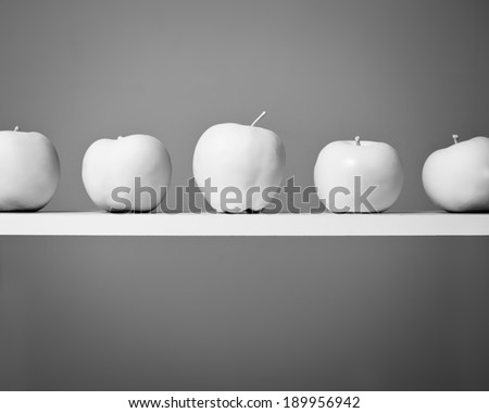 White Apples in a Row. A line of painted white apples sit on a shelf. Black and White.