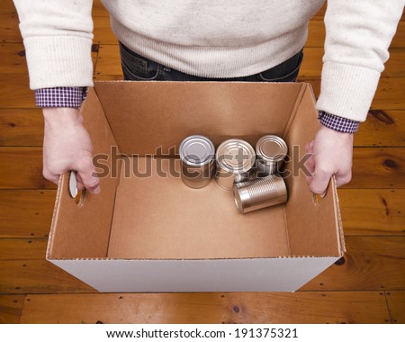 A man holding a cardboard box containing a few tin cans for a food drive.