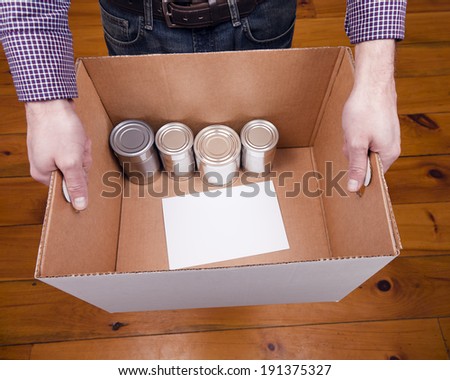 A man holding a cardboard box containing a few tin cans for a food drive.
