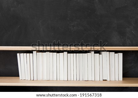 White Books Shelf on Blackboard. A row of all white books sit on a shelf in front of a chalkboard.