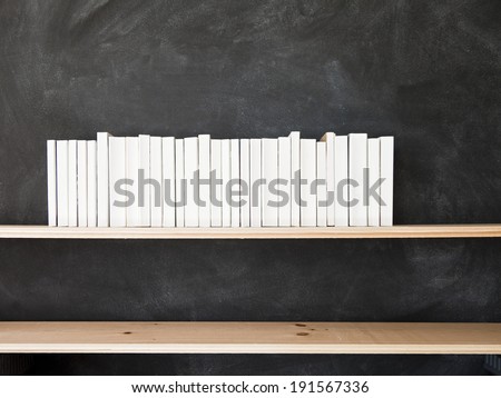 White Books Shelf on Blackboard. A row of all white books sit on a shelf in front of a chalkboard.
