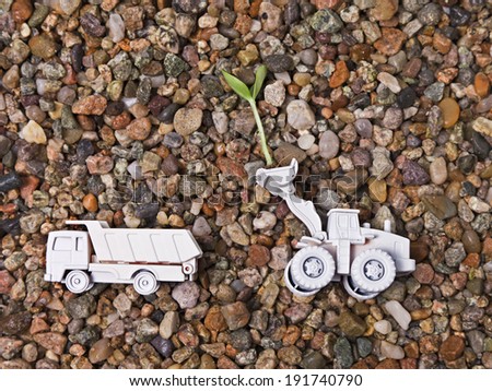 Loading Plant Sprout. Two all white toy construction vehicles against a gravel background.