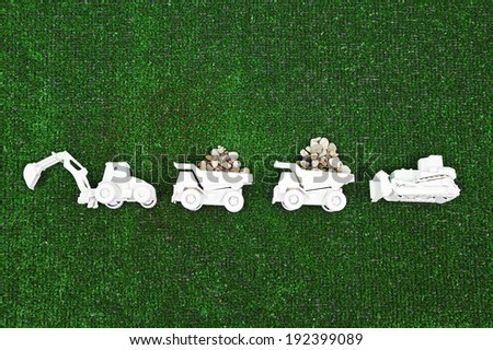 A row of white construction vehicles against a green turf background with piles of rocks in the white dump trucks.