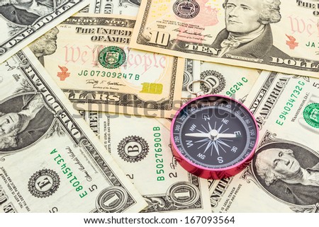 Closeup of compass on a heap of paper dollars.