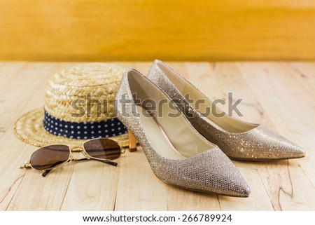 Modern style image of female fashion: straw hat, sun glasses and high heel of golden shoes on wooden background.