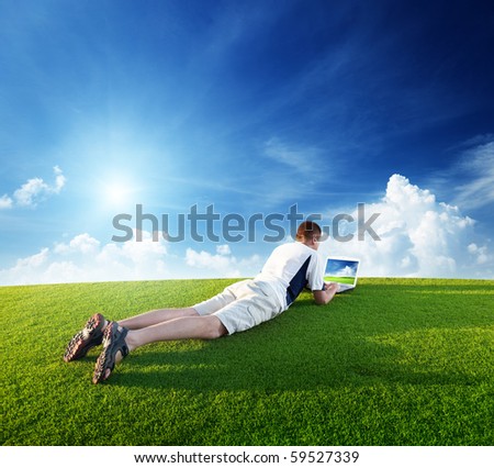 Young man use a notebook on green field