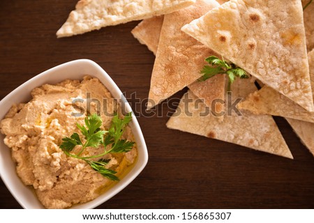 Hummus in a bowl with parsley and olive oil on it, next to pita bread.
