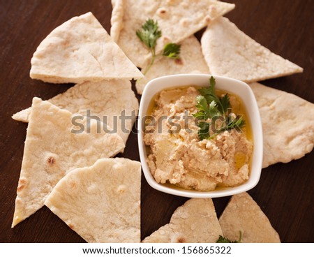 Hummus in a bowl with parsley and olive oil on it, next to pita bread.