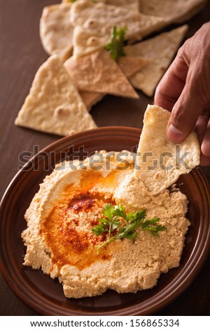 Close up of human hand dipping hummus with pita bread.