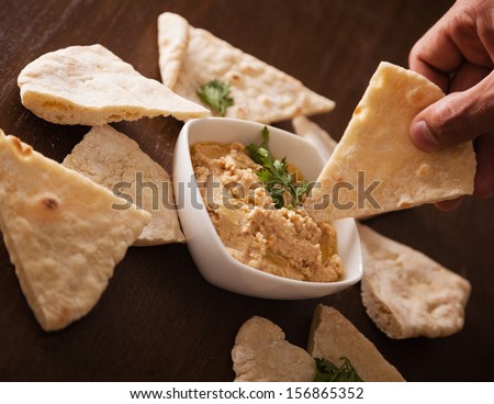Close up of human hand dipping hummus with pita bread.