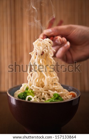 Close up of human hand grabbing noodles with chopsticks from a bowl with hot noodle soup.