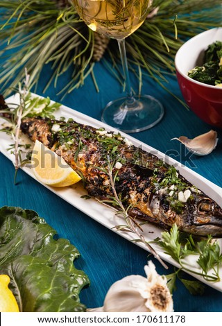 Grilled fish on white plate with lemon, garlic and rosemary.
