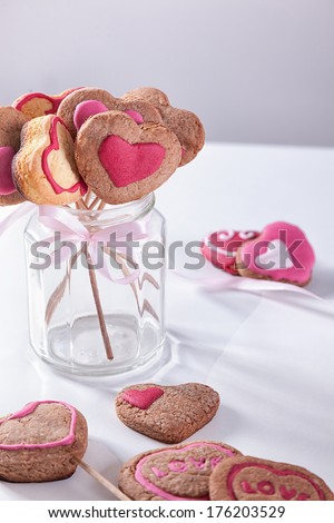 Homemade heart shape cookies on a stick in a glass.