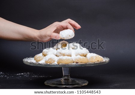 A big glass serving plate full of Kahk covered with sugar powder (traditional Arabian cookies) and a female hand is grabbing of the cookies
