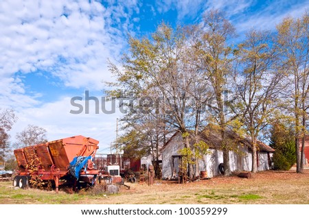 A rusting cotton trailer stands next to disused machinery and an old farm building in rural Georgia.