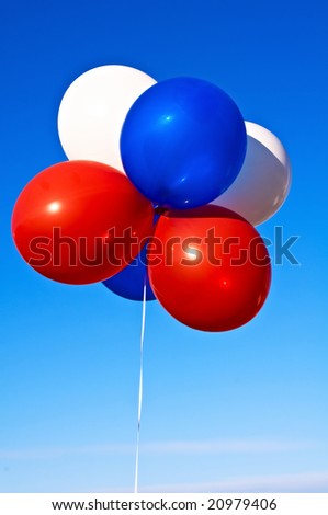 A bunch of party balloons in patriotic colors in the sunshine against a blue sky.