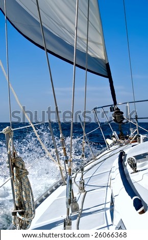 A sailboat with reefed jib is hard on the wind, heading towards the open ocean creating spray.