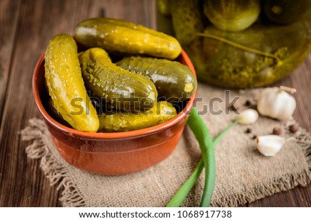 Pickled cucumbers in bowl on wooden rustic table with garlic and jar of pickles.