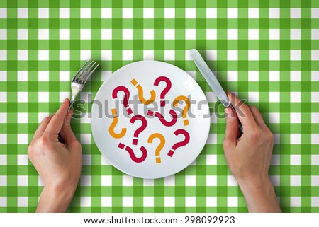 Top view of woman's hands at dining table holding a fork and knife above dish with question marks. Food concept.