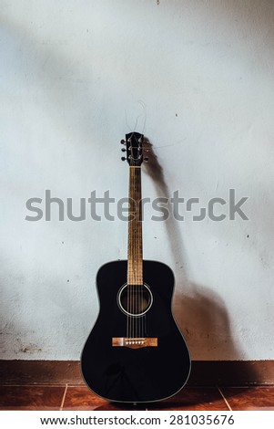 black acoustic guitar in front of a vintage wall