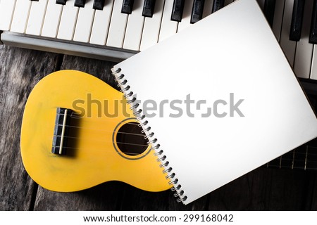 note book with piano key and ukulele on a wooden floor.