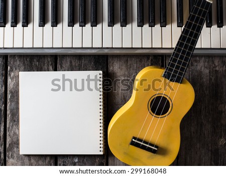 note book with piano key and ukulele on a wooden floor.