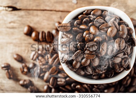 smoke of coffee beans on cup with coffee beans, on wood background