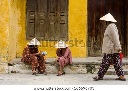 12 JUNE 2011 - HOI AN, VIETNAM - Women in traditional clothing and cone hats count their money by the street, on 12 June 2011, in Hoi An, Vietnam