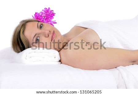 Spa therapy pretty young blond woman looking at camera, partial nude enjoying aroma therapy covered with towel laying on massage table. In studio on white background.
