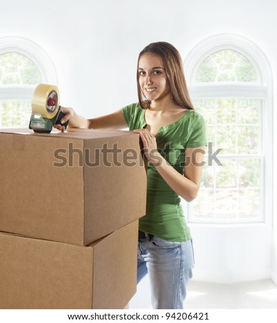 Young woman moving into a new home and is moving, taping and unpacking boxes. Soft background.