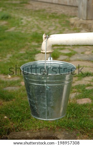 Silver bucket full of water hanging on pump