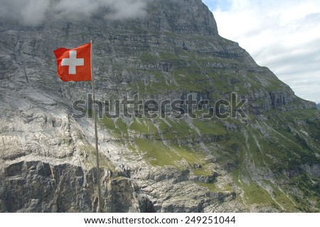 Swiss flag fluttering on wind high in mountains nearby Grindelwald in Alps in Switzerland.