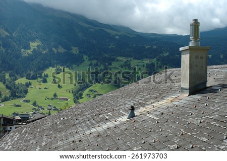 Chimney on roof covered with shingles and cloudy mountain view