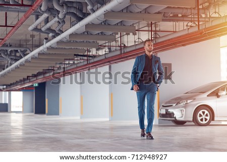 Confident look. Full length of a professional confident businessman walking along the parking lot after having parked his car
