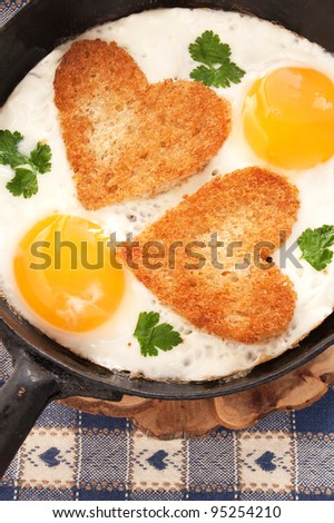 fried eggs with slices of bread in the shape of a heart in the frying pan