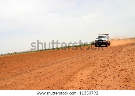 Red Australian rural road with approaching white off road car.Tanami road, Western Australia