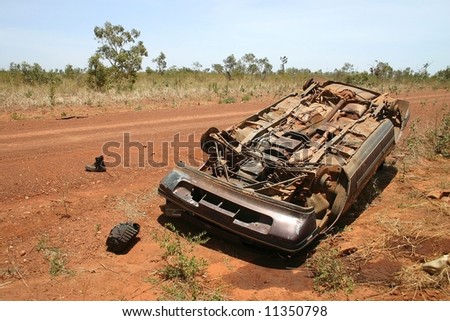 Australian red rural road with an overturned obsolete rusted car on the roadside. Pollution Damage. Tanami road, Western Australia