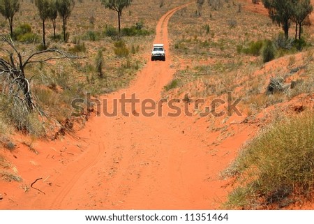 Red Australian wild road with approaching white off road car. Northern Territory, Australia