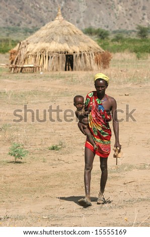 KENYA - FEBRUARY 27: Man carrying a child across the village with traditional huts. Great trekking February 27, 2004 in Kenya.