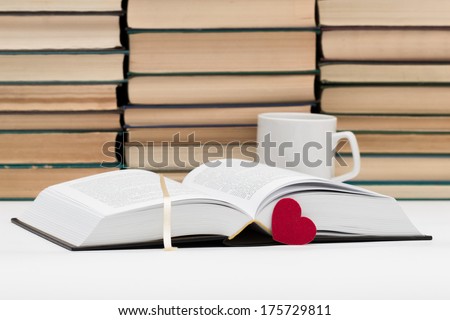 The opened book and red heart against piles of books and a cup